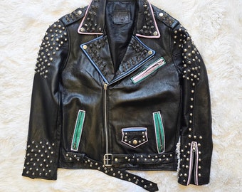 May include: Black leather jacket with silver studs, pink and green trim, and a zipper closure. The jacket has a belt with silver studs.