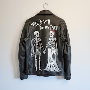 Könnte beinhalten: Schwarze Lederjacke mit weißem Skelettpaar, das sich an den Händen hält. Auf der Rückseite steht der Text "Till Death Do Us Part". Die Skelettbraut hat einen roten Akzent auf dem Kopf.