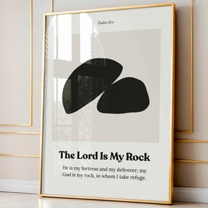 May include: Framed art print with a gold border. The artwork features two abstract black shapes on a light gray background. The text "Psalm 18:2" is at the top, and "The Lord Is My Rock" is at the bottom, with a Bible verse below.
