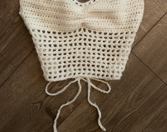 May include: White crochet top with a criss-cross halter neckline and a tie at the bottom.