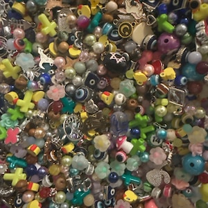 May include: A large assortment of colorful beads and charms, including crosses, flowers, stars, and evil eye charms. The beads are made of various materials, including glass, metal, and plastic.