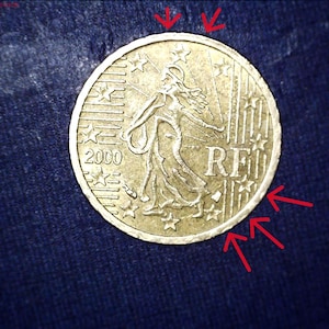 May include: A gold-coloured 2000 French 20-cent euro coin. The coin shows a woman with outstretched arms, surrounded by stars. The letters "RF" are visible on the coin.