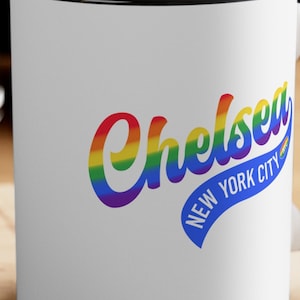 May include: White ceramic mug with a black rim and handle. The mug features a rainbow-colored graphic of the word "Chelsea" with the text "New York City" in a blue ribbon below.