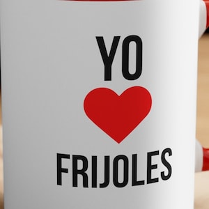 May include: White ceramic mug with a red rim and handle. The mug has black text that says "YO ♥ FRIJOLES".