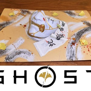 May include: A decorative plate with a white mask, a white cloth with Japanese characters, and yellow leaf accents. The plate has a beige background with black and white brushstrokes and red paint splatters. The word "GHOST" is at the bottom.