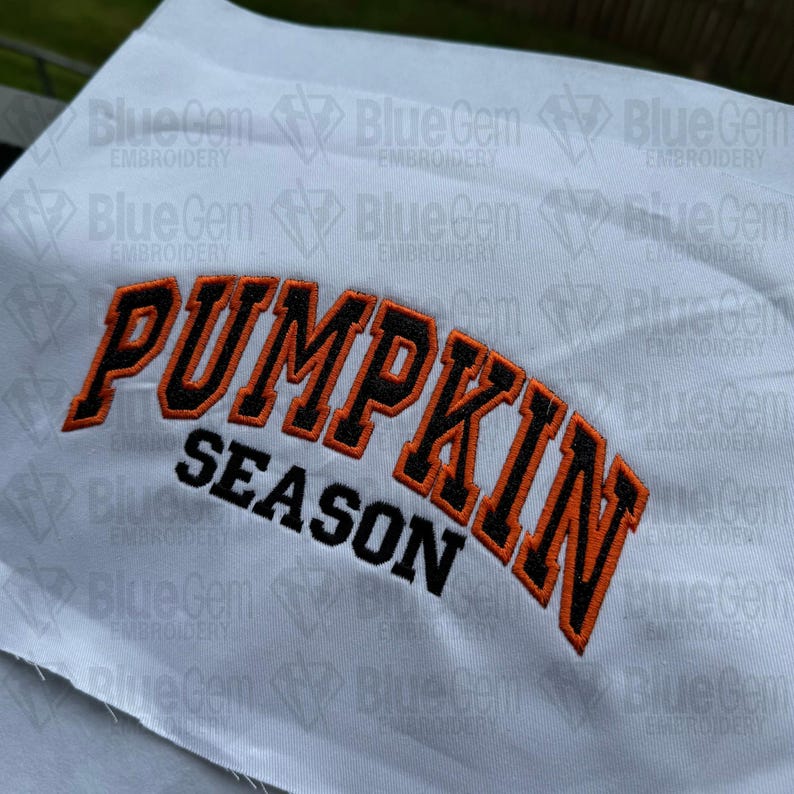 May include: White fabric with orange and black embroidered text that reads "PUMPKIN SEASON".