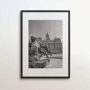 May include: Black and white photograph of a statue of a man riding a horse in front of a building. The statue is in a fountain and the building is in the background.