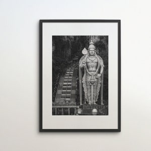 May include: Black and white framed print of a large statue of a deity, holding a spear, standing before a long staircase. The statue is detailed with ornate carvings. The print is displayed on a white wall.