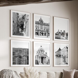 Puede incluir: Un salón con un sofá seccional beige, una mesa de centro redonda y una ventana grande. Seis impresiones en blanco y negro enmarcadas de ciudades cuelgan en la pared. Una manta acogedora y cojines decorativos añaden calidez.