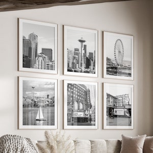 May include: A living room with a white couch and a coffee table. There are six black and white framed photos on the wall, featuring cityscapes and a Ferris wheel. The room has a large window with a view of trees.
