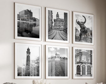 May include: A living room interior with a white couch, a coffee table, and a white ottoman. The walls are decorated with black and white framed photographs of cityscapes.