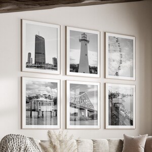 Op de afbeelding: Een woonkamerinterieur met een witte bank, een ronde salontafel en een witte poef. De kamer is versierd met zwart-witte ingelijste foto's van stadsgezichten en bruggen.