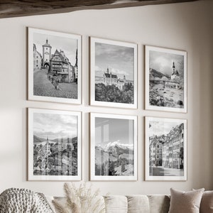 Könnte beinhalten: Ein Wohnzimmer-Interieur mit einem weißen Sofa, einem Couchtisch und einem weißen Hocker. Sechs schwarz-weiße gerahmte Fotografien von europäischen Stadtansichten hängen an der Wand.