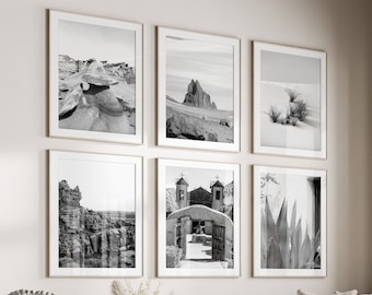 May include: A living room interior with a white sofa and a coffee table. The walls are decorated with six black and white framed photographs of desert landscapes and architecture. A large window with wooden trim looks out onto a green lawn.