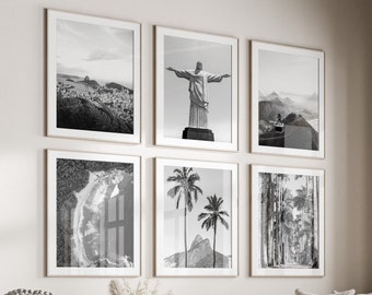 May include: A living room interior with a white sectional sofa, a round coffee table, and a white ottoman. The walls are white and feature a gallery wall of six black and white framed photographs. The window is framed in dark wood and has a view of green trees.