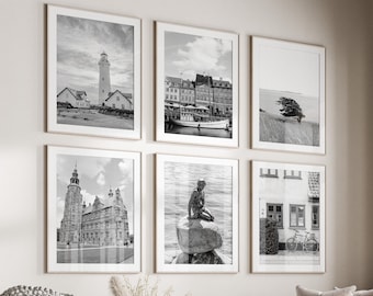 May include: A living room interior with a white couch, a coffee table, and a white ottoman. Six black and white framed photographs are hung on the wall above the couch. The photographs depict various scenes of a city, including a lighthouse, a harbor, and a statue.