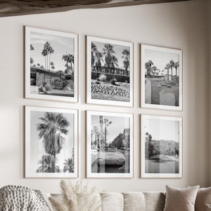 Può includere: Un interno di soggiorno con un divano bianco, un tavolino da caffè e un pouf bianco. Le pareti sono bianche e ci sono sei fotografie incorniciate in bianco e nero di palme e un'auto sul muro. C'è una finestra con vista sugli alberi e una cornice in legno.