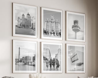 May include: A living room with a white couch and a coffee table. There are six black and white framed photos on the wall, featuring various cityscapes. The room has a large window with a view of trees and a wooden floor.