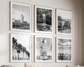 May include: A living room interior with a white couch, a round coffee table, and a white ottoman. The walls are decorated with black and white framed photographs of various landscapes and cityscapes. The room has a large window with a view of trees outside.