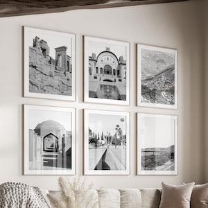 May include: A living room interior with a white couch, a white coffee table, and a white ottoman. The room has a large window with a view of trees and a white wall with six black and white framed photographs of various architectural scenes.