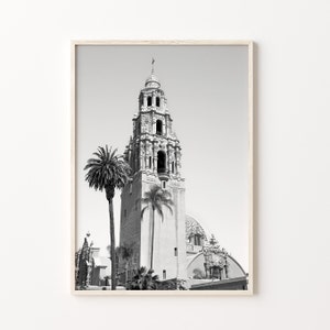 Op de afbeelding: Zwart-witfoto van een hoog, versierd gebouw met een klokkentoren. Het gebouw wordt omringd door palmbomen.