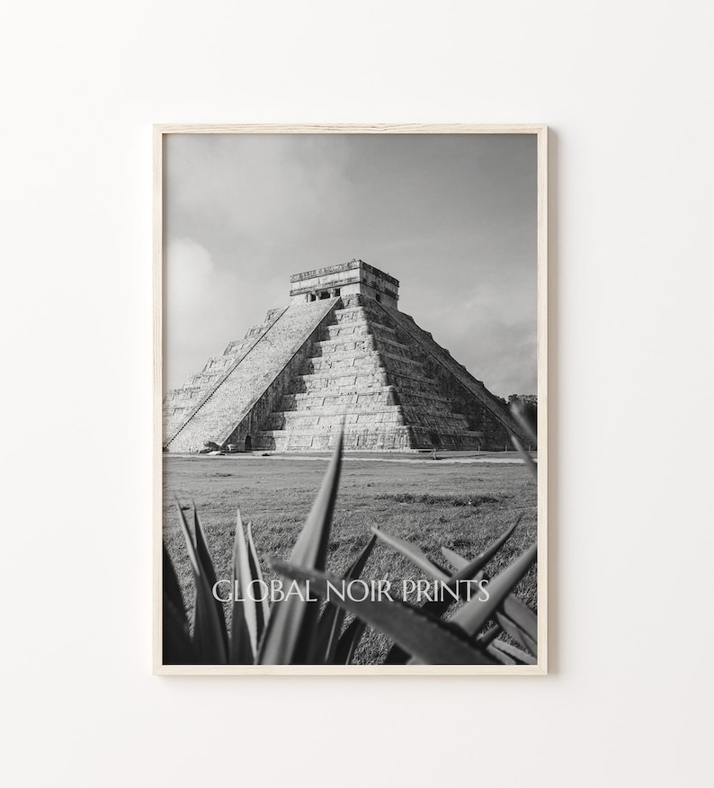 May include: Black and white photograph of the Mayan pyramid, Chichen Itza, in Mexico. The pyramid is made of stone and has a series of steps leading to the top. The pyramid is surrounded by grass and trees.