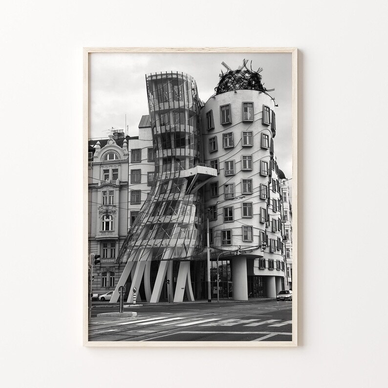 May include: Monochrome photograph of a modern building with a distinctive, curved glass facade. The building features a tower-like structure and a wavy design. The image is framed in a light wood frame, suitable for home decor.