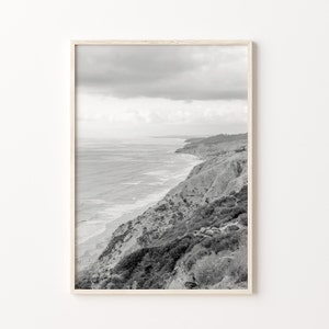 Op de afbeelding: Een zwart-witfoto van een rotsachtige kustlijn met de oceaan op de achtergrond. De foto is gemaakt vanaf een hoog standpunt, met uitzicht op de oceaan en de kliffen.