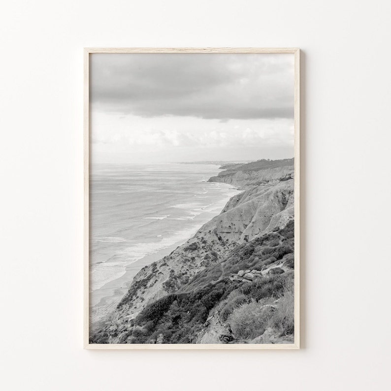 Op de afbeelding: Een zwart-witfoto van een rotsachtige kustlijn met de oceaan op de achtergrond. De foto is gemaakt vanaf een hoog standpunt, met uitzicht op de oceaan en de kliffen.