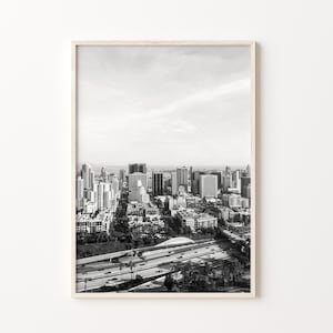 Op de afbeelding: Zwart-witfoto van een skyline met een snelweg op de voorgrond. De stad is in de verte en de snelweg is op de voorgrond. De foto is genomen vanuit een hoog standpunt.