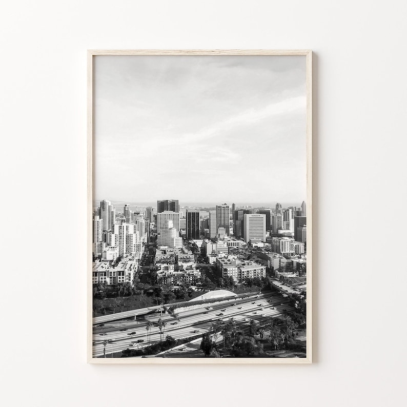Op de afbeelding: Zwart-witfoto van een skyline met een snelweg op de voorgrond. De stad is in de verte en de snelweg is op de voorgrond. De foto is genomen vanuit een hoog standpunt.