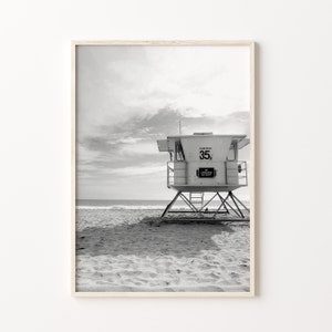 Op de afbeelding: Zwart-witfoto van een reddingsbrigadepost op een zandstrand. De post heeft een bord met de tekst "Carlsbad 35" en "Geen badmeester aanwezig".