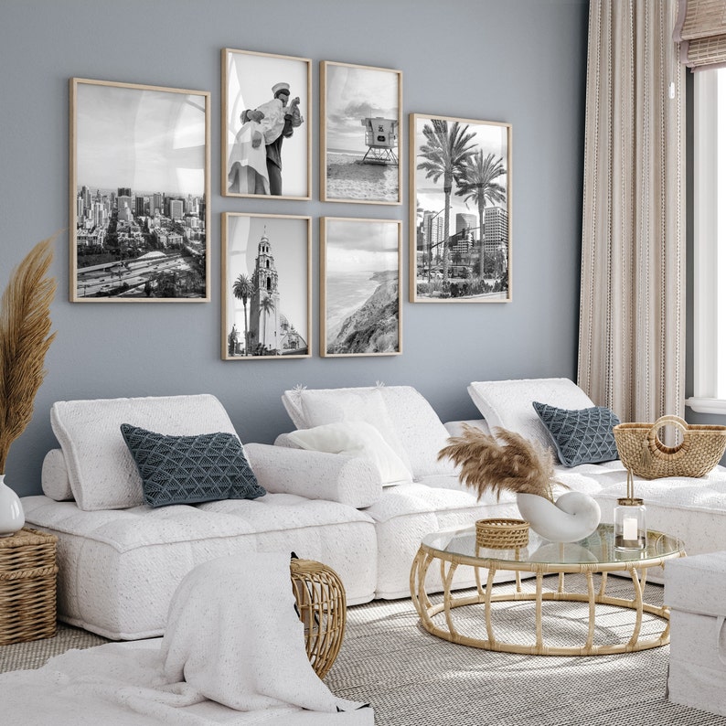 Op de afbeelding: Een woonkamer met een witte modulaire bank, een glazen salontafel met een gevlochten basis en een set zwart-wit geframed foto's aan de muur. De foto's tonen stadsgezichten, palmbomen en een strandsc&egrave;ne.