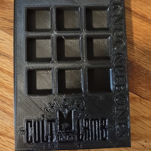 May include: Black plastic storage box with 12 square compartments. The box has the words "KNUCKLEBONES" printed vertically on the right side and "CULT OF THE CROWN" printed on the bottom.