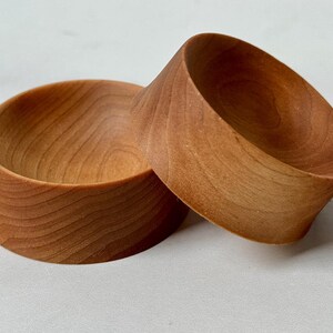 Puede incluir: Dos cuencos de madera, uno apilado sobre el otro. Los cuencos son de madera marr&oacute;n claro y tienen una forma redonda y lisa.