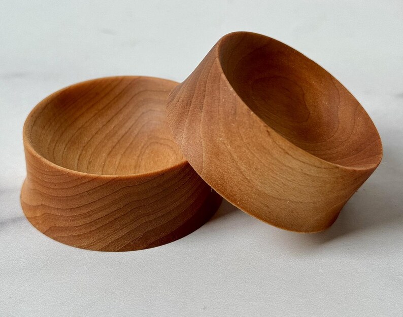 Puede incluir: Dos cuencos de madera, uno apilado sobre el otro. Los cuencos son de madera marr&oacute;n claro y tienen una forma redonda y lisa.