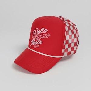 May include: A red trucker hat featuring a white cord across the brim and a white mesh back with a red and white checkered pattern. The front panel displays the white embroidered text Delta Sigma Theta 1913 in a cursive script font style.