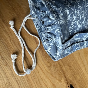 May include: A blue drawstring bag with a white floral pattern. The bag has a white drawstring and a white toggle.