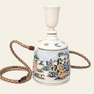 May include: A ceramic hookah base featuring a hand-painted desert scene with figures in traditional attire, a crescent moon, and stars. The white vessel has a cylindrical shape, a top socket, and a flexible brown woven hose with a dark tip.