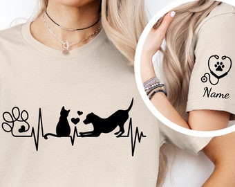 May include: Beige t-shirt with a black paw print, heartbeat, cat, and dog graphic. The sleeve has a black stethoscope with a paw print in a heart and the text "Name".