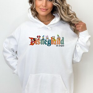 Puede incluir: Sudadera con capucha blanca con un logotipo de Disneyland colorido que presenta a Mickey Mouse, Minnie Mouse, Donald Duck, Goofy y Pluto. El texto debajo del logotipo dice "The Original."