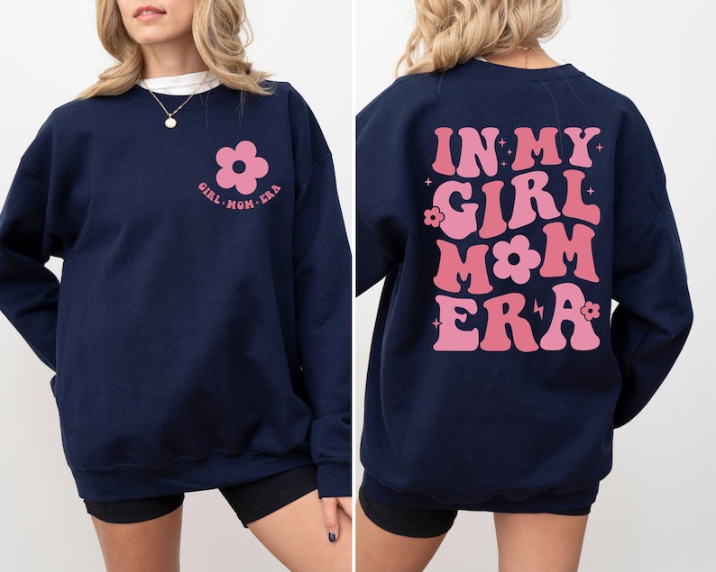 Puede incluir: Sudadera azul marino con el texto "GIRL MOM ERA" y un gr&aacute;fico de flores rosas en la parte delantera. La parte trasera de la sudadera presenta el texto "IN MY GIRL MOM ERA" en rosa, con letras de estilo retro. Una prenda superior informal y c&oacute;moda.