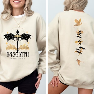May include: A beige sweatshirt with a black dragon graphic on the front and the text "BASGIATH - WAR COLLEGE" below. The back of the sweatshirt has a gold dragon graphic and the text "Fly or Die".