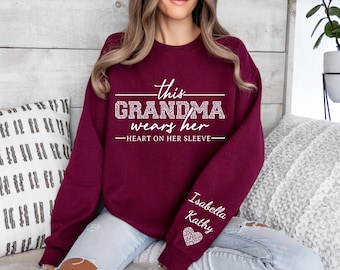 May include: Burgundy sweatshirt with the text "This Grandma wears her heart on her sleeve" and the names "Isabella" and "Kathy" on the sleeve.