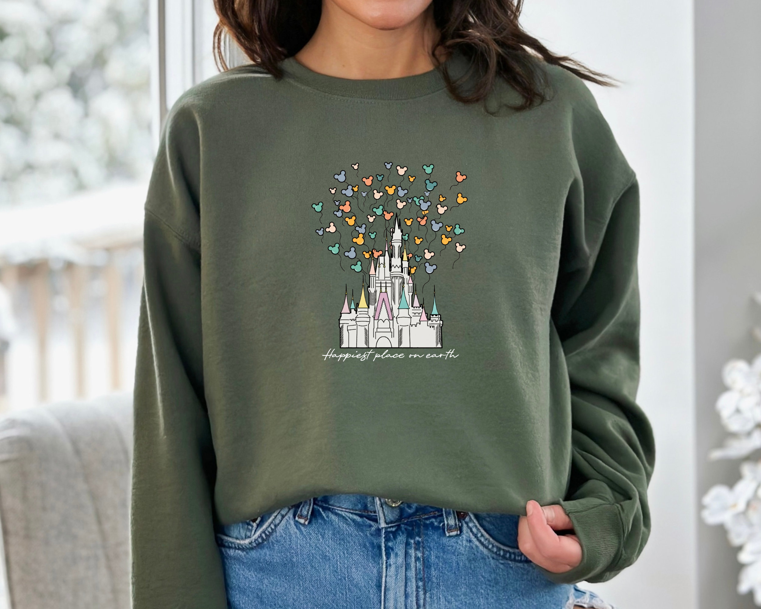 May include: A green sweatshirt with a white graphic of Cinderella's castle with colorful Mickey Mouse balloons and the text "Happiest place on earth".