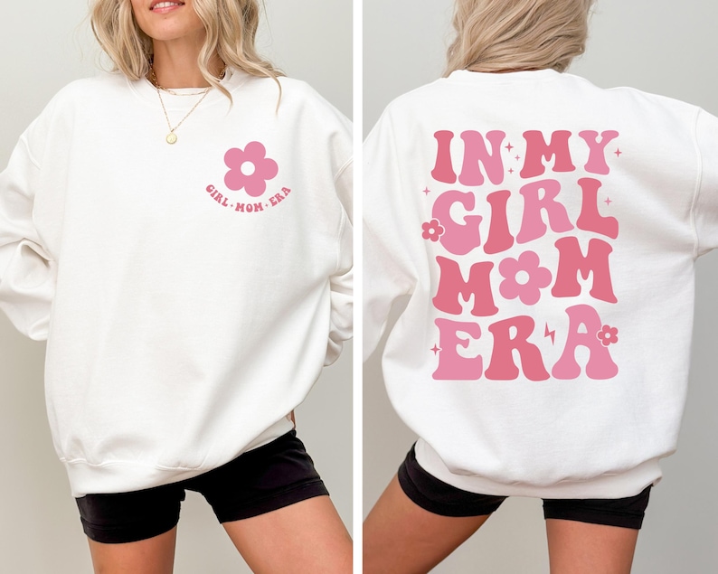 Puede incluir: Sudadera blanca con el texto "GIRL MOM ERA" y un gr&aacute;fico de flores rosas en la parte delantera. La parte trasera de la sudadera presenta la frase "IN MY GIRL MOM ERA" en rosa.
