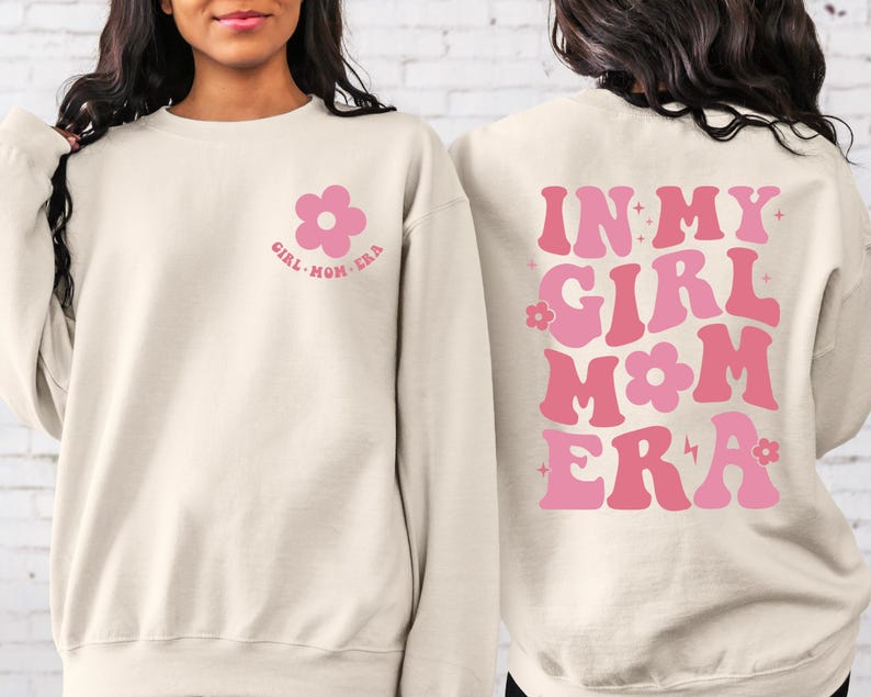 Puede incluir: Sudadera color crema con gr&aacute;ficos florales rosas. La parte delantera presenta una flor y el texto "GIRL MOM ERA". La parte trasera muestra "IN MY GIRL MOM ERA" en letras rosas.