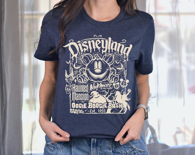 Puede incluir: Camiseta azul marino con un dise&ntilde;o gr&aacute;fico color crema. El dise&ntilde;o incluye la palabra "Disneyland" en una fuente estilizada, junto con una calabaza, Mickey Mouse y el texto "Haunted Nightmare" y "Oogie Boogie Bash Est. 1955".