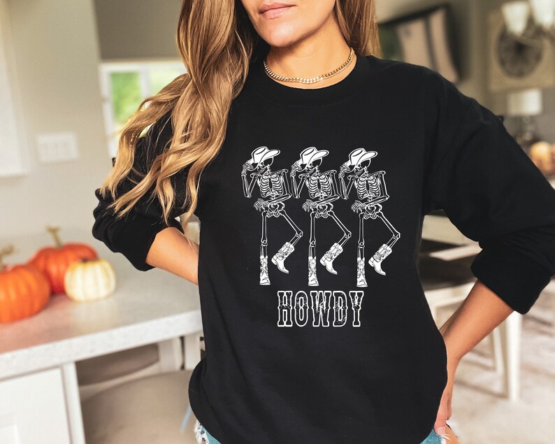 May include: Black sweatshirt with a white graphic of three skeletons wearing cowboy hats and boots. The text "HOWDY" is printed below the skeletons.