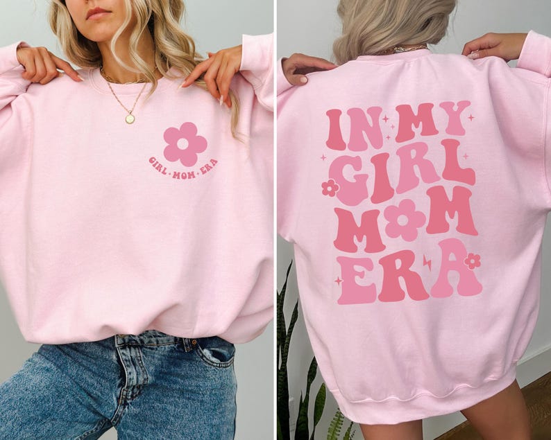 Puede incluir: Una sudadera rosa claro con el texto "IN MY GIRL MOM ERA" en tonos rosas en la espalda. La parte delantera presenta un gr&aacute;fico de flores y el texto "GIRL MOM ERA".